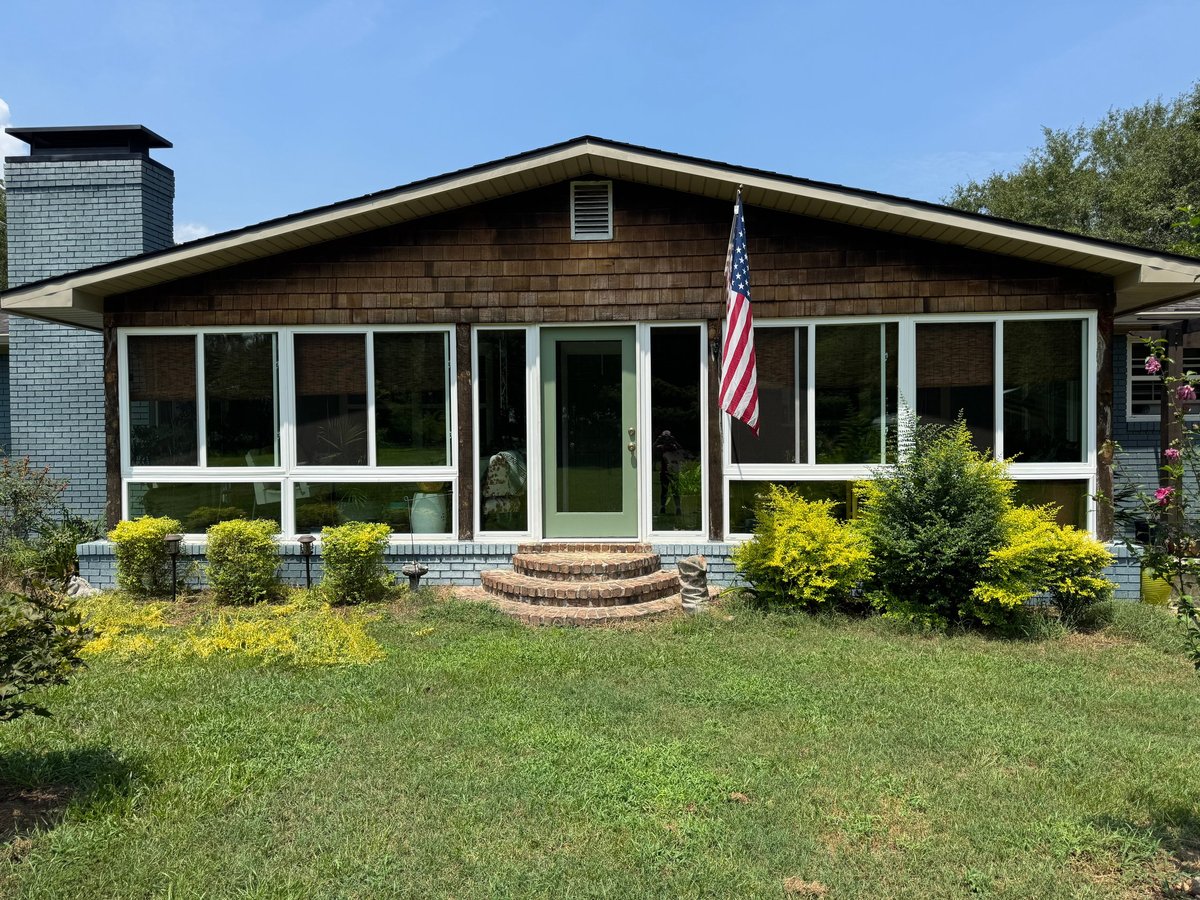 Front view of a single-story brown brick ranch house with white-trimmed windows, an American flag, and landscaped shrubs